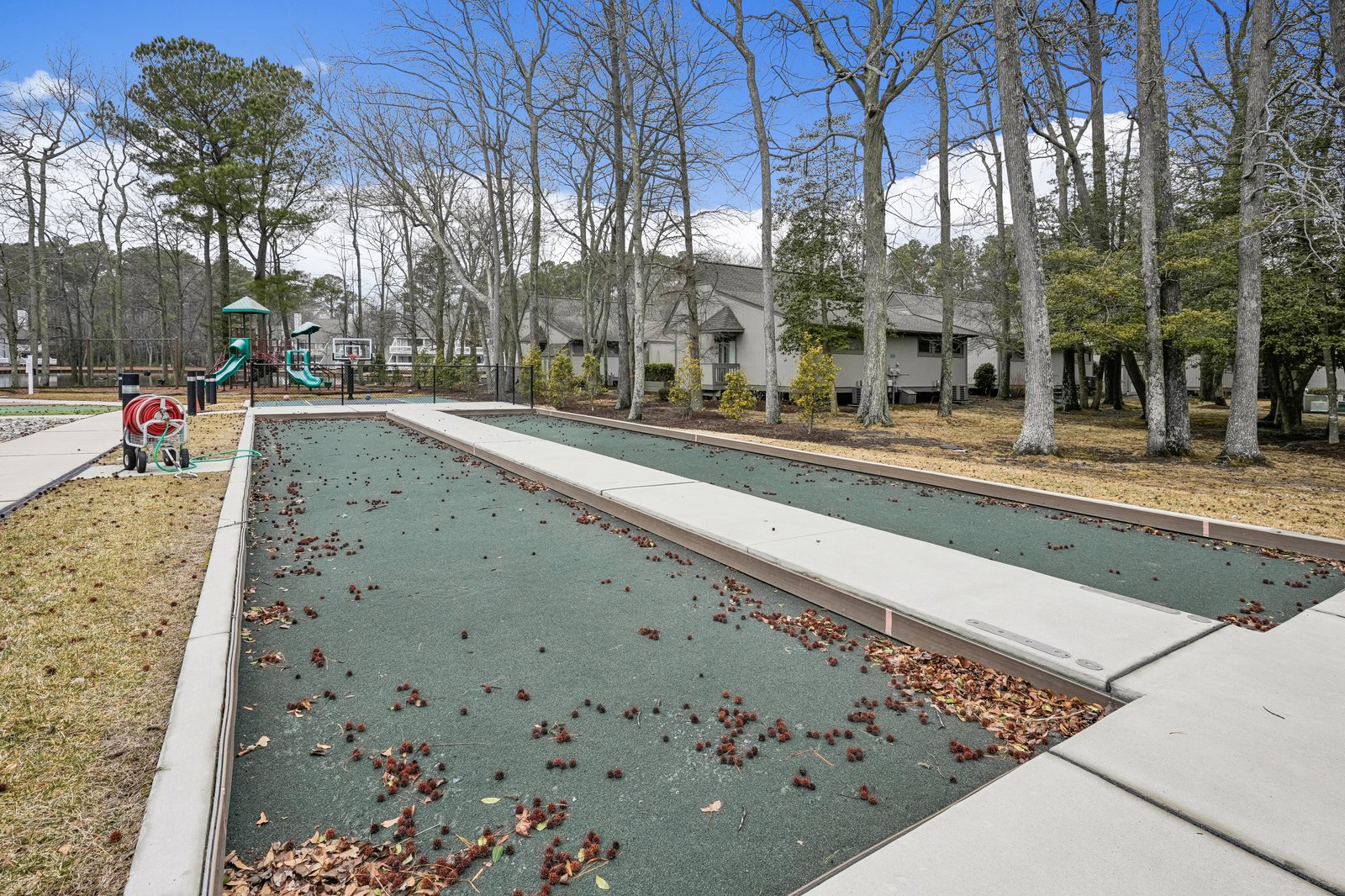 Bocce ball court and playground nestled among tall trees, offering outdoor recreation within the property's leafy, peaceful setting.