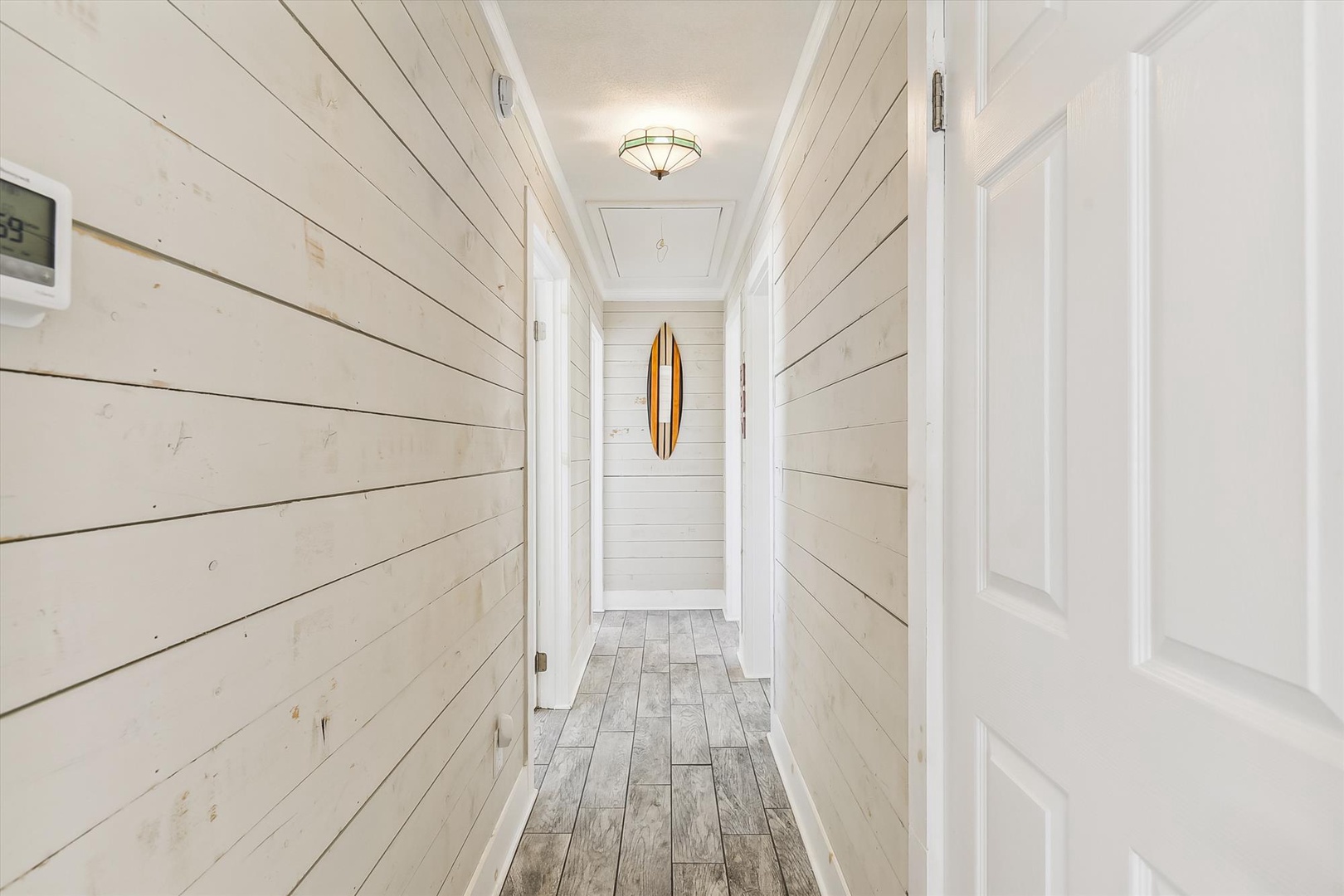 Whitewashed shiplap walls and weathered wood floors create a serene coastal vibe, while the vintage surfboard at the end of the hall adds a playful beachy touch to your hallway.