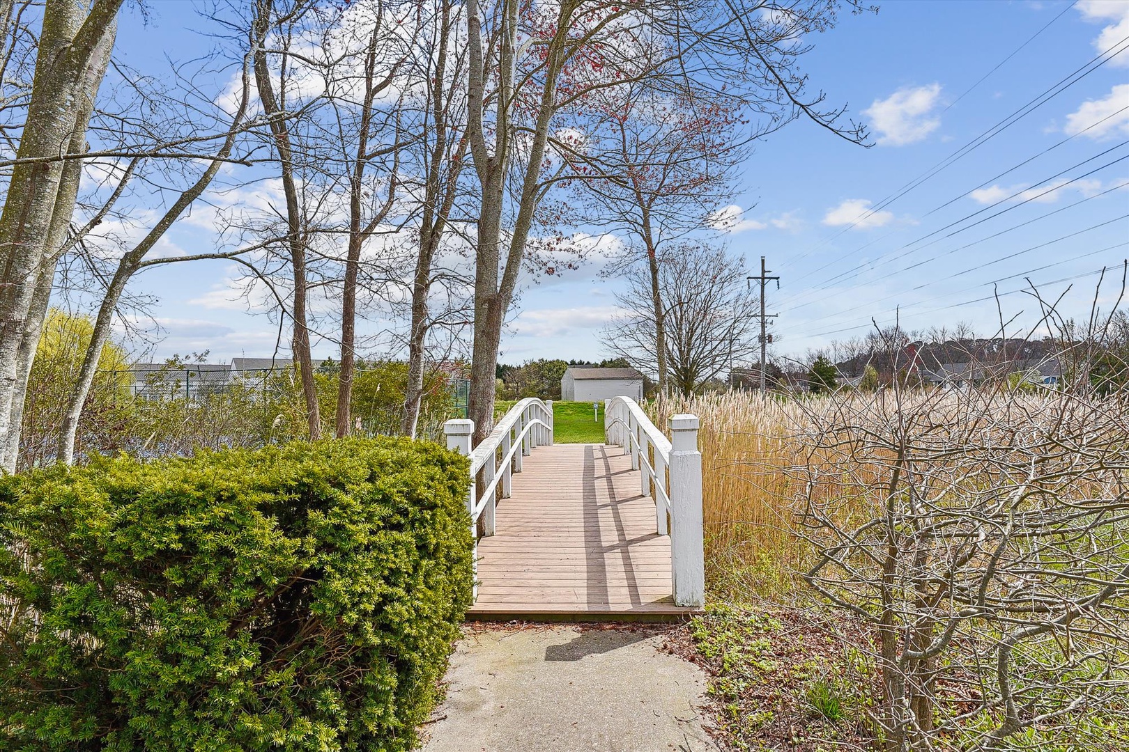 A charming white footbridge leads through lush greenery and natural landscape, offering a peaceful pathway near the property's tranquil waterfront surroundings.