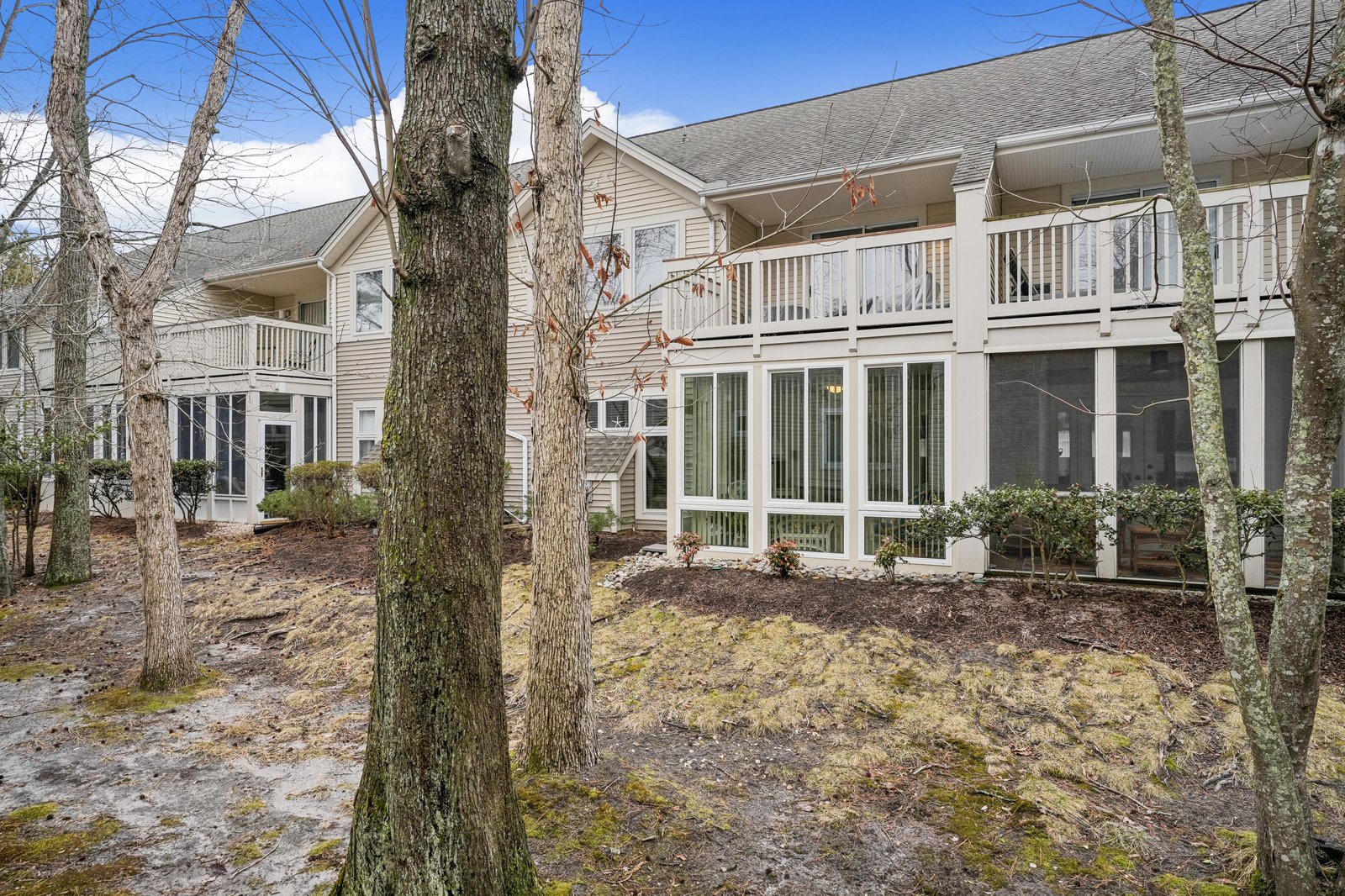 Two-story vacation rental building featuring screened porches and private balconies, surrounded by mature trees in a peaceful woodland setting.