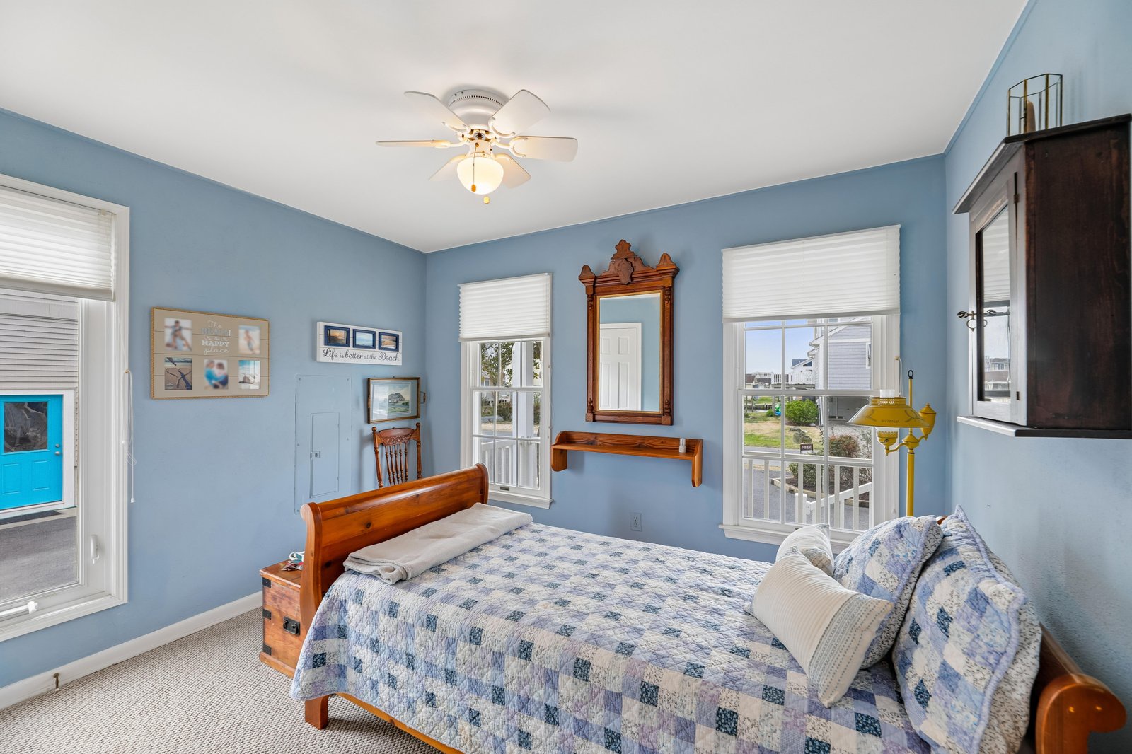 Your bright, breezy bedroom features soothing blue walls, a cozy bed with coastal charm, and windows that flood the space with natural light—perfect for unwinding after a day of seaside adventures.