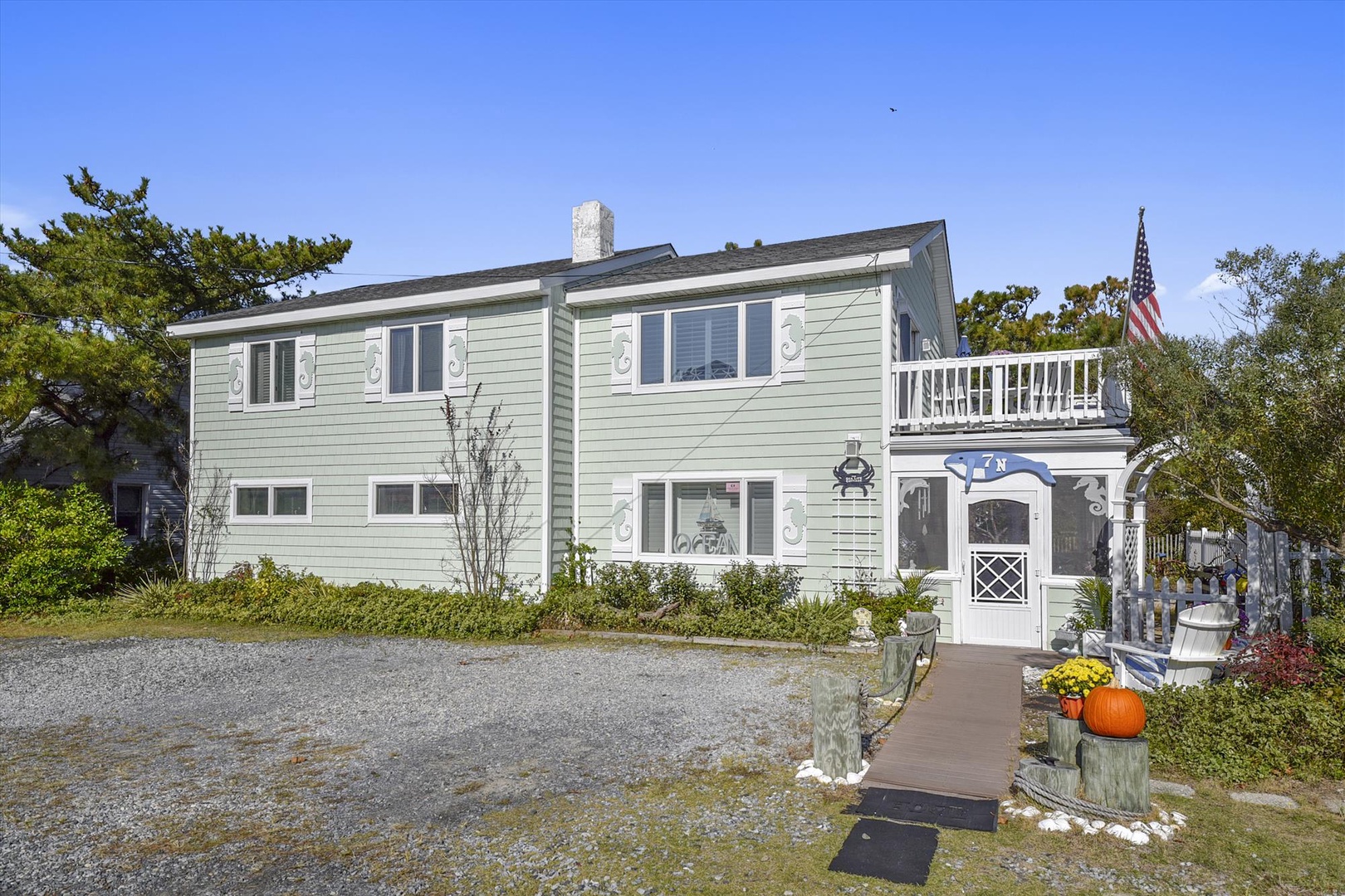 Charming coastal property with welcoming entrance, private balcony, and gravel parking set among lush greenery. Classic beach house design with convenient outdoor access.