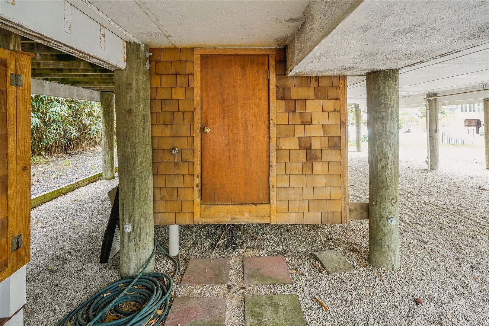Ground-level entrance with rustic cedar shingle siding and wooden door, offering sheltered access beneath the property with nearby parking area.