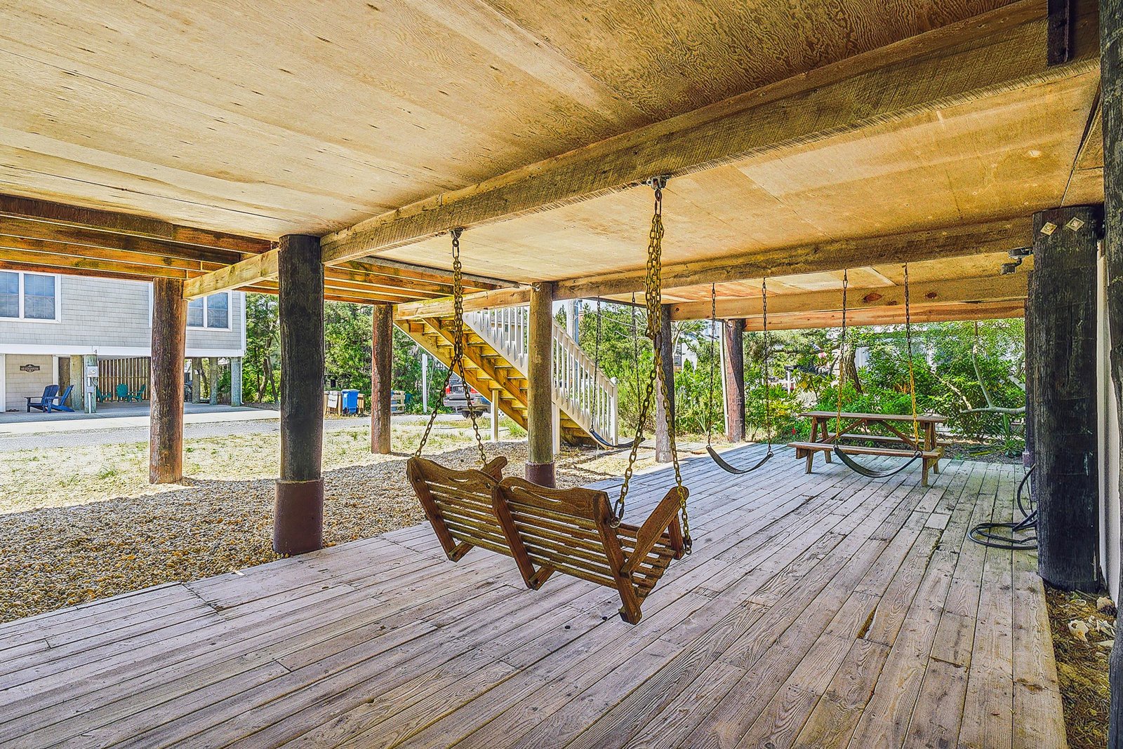 A shaded covered area beneath the property with wooden porch swings invites leisurely moments overlooking the coastal surroundings.