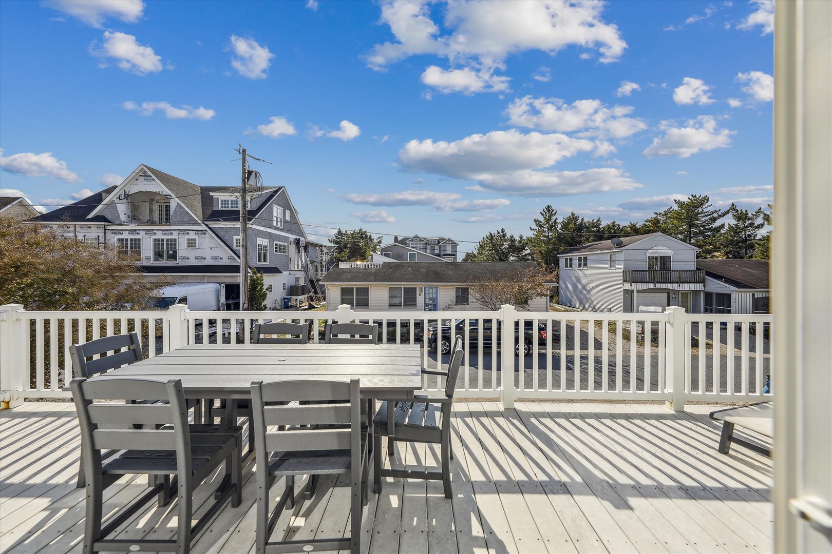 A spacious white deck with outdoor dining overlooking a quiet coastal neighborhood, framed by blue skies and soft clouds—ideal for morning coffee or sunset meals.