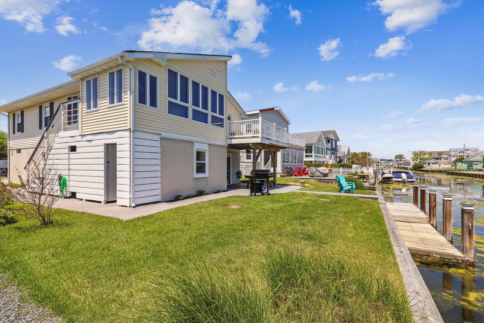 Waterfront vacation home featuring spacious backyard with private dock access, BBQ facilities, and expansive lawn area perfect for outdoor relaxation and canal views.