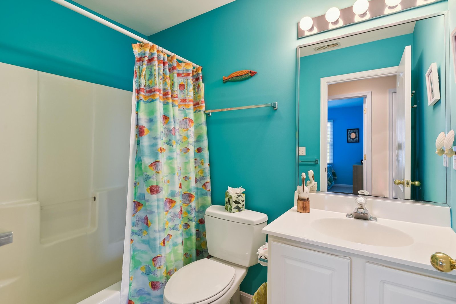 Refresh in this cheerful, tropical-themed bathroom with playful fish details and bright turquoise walls that echo coastal vibes.