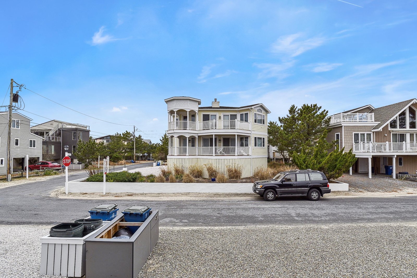 A spacious two-story coastal property with wrap-around balconies, surrounded by natural dune landscaping and located on a quiet residential corner.