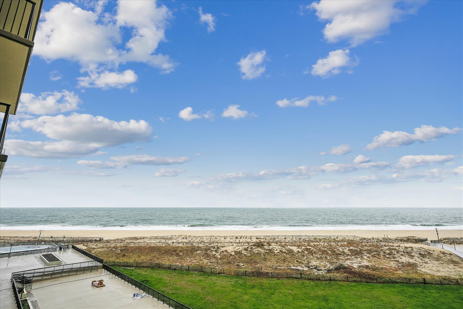 The property offers direct beachfront access with expansive coastal views, green lawn areas, and sandy shoreline meeting calm ocean waters under open skies.