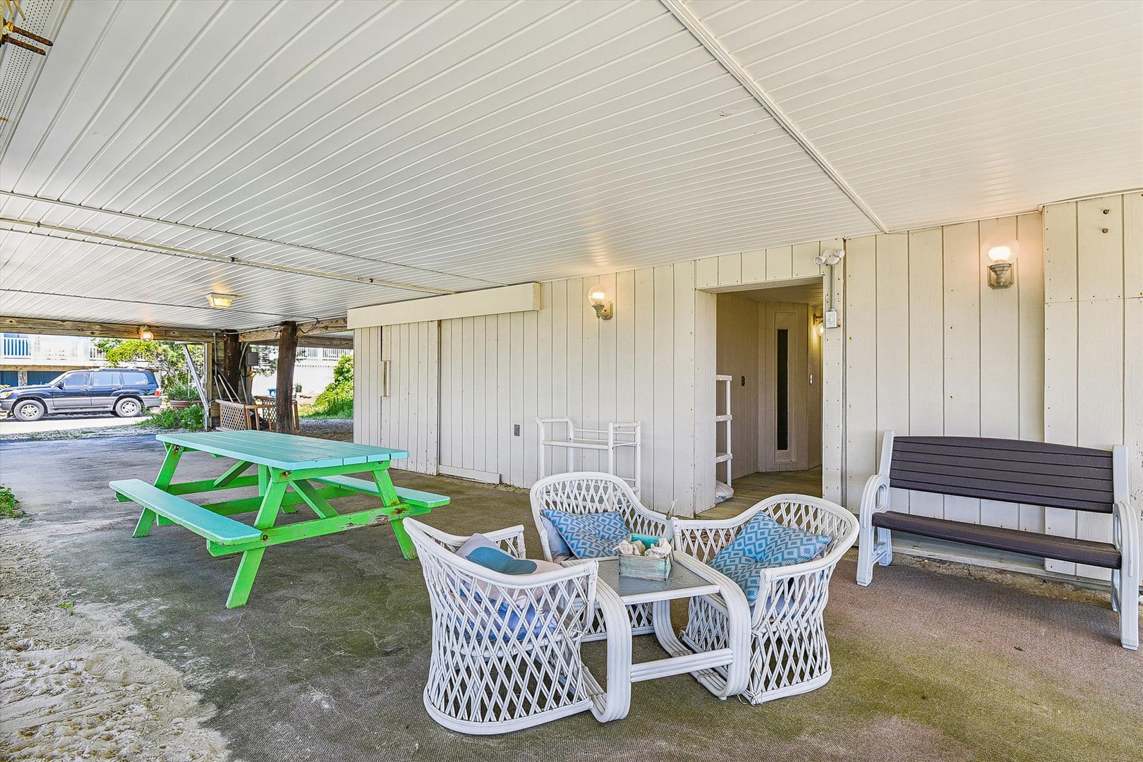 The covered patio with casual seating and bright green picnic table provides a sheltered entrance area to the property, visible just beyond the residential neighborhood street.
