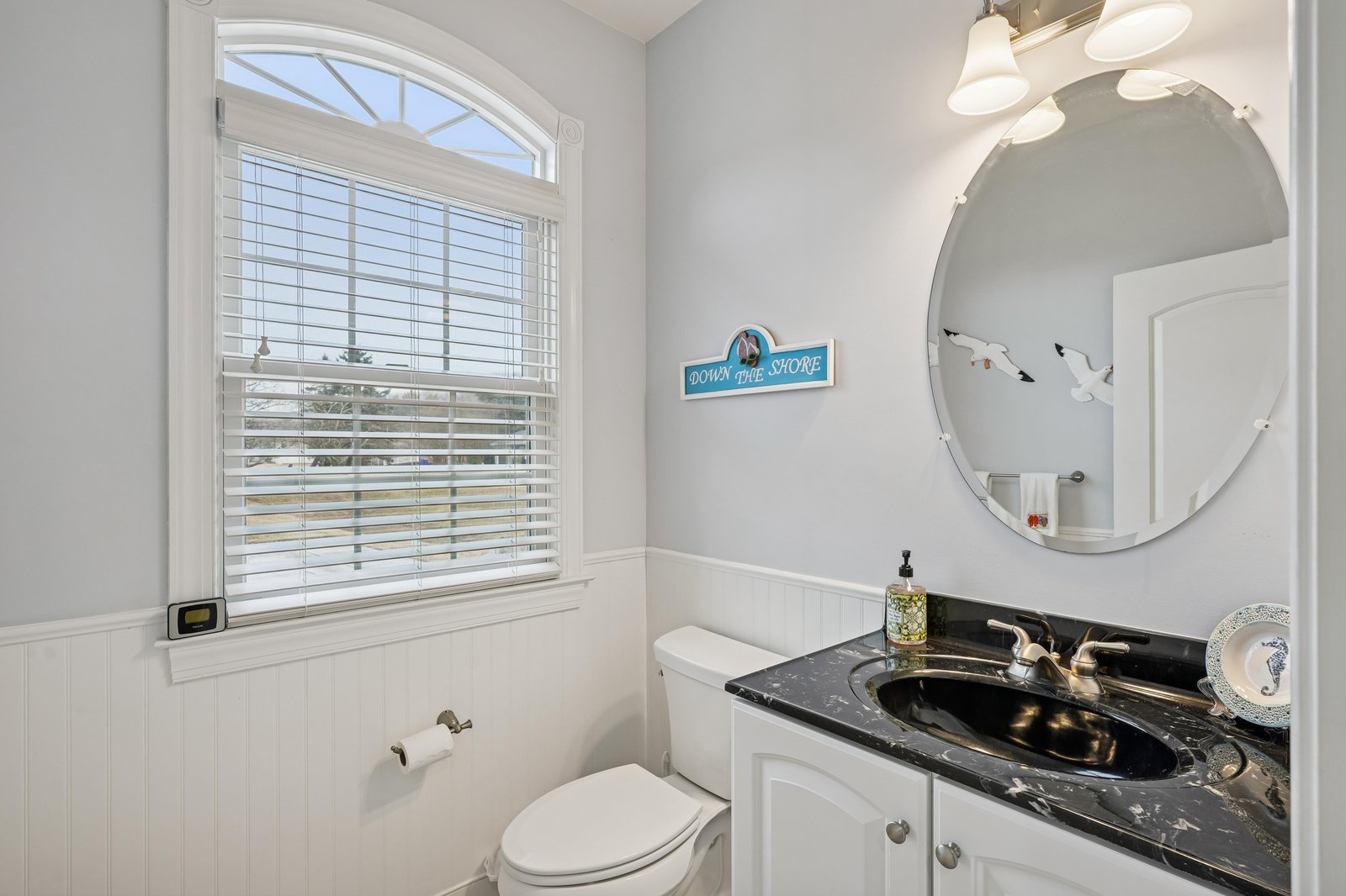 Step into a bright, beach-themed bathroom with coastal charm. White wainscoting and soft blue walls create a serene atmosphere while the gleaming marble vanity adds a touch of elegance to your stay.