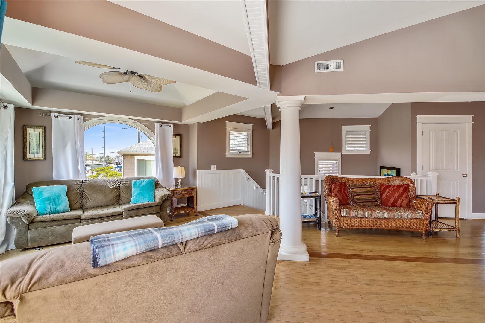 Unwind in your spacious living room with soaring vaulted ceilings, cozy seating, and natural light streaming through arched windows. The warm hardwood floors and coastal breeze invite you to relax and feel right at home.