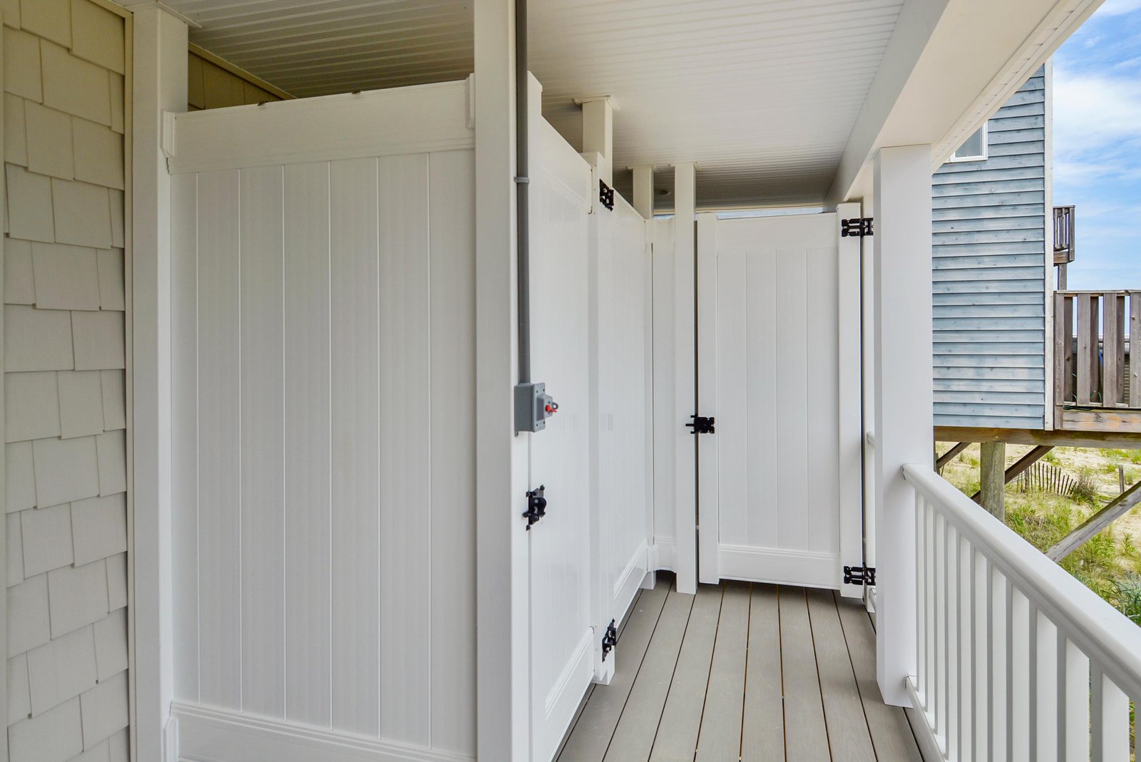 An outdoor shower on a covered porch, with wooden plank walls and floors, providing a convenient way to rinse off after a day at the nearby beach.