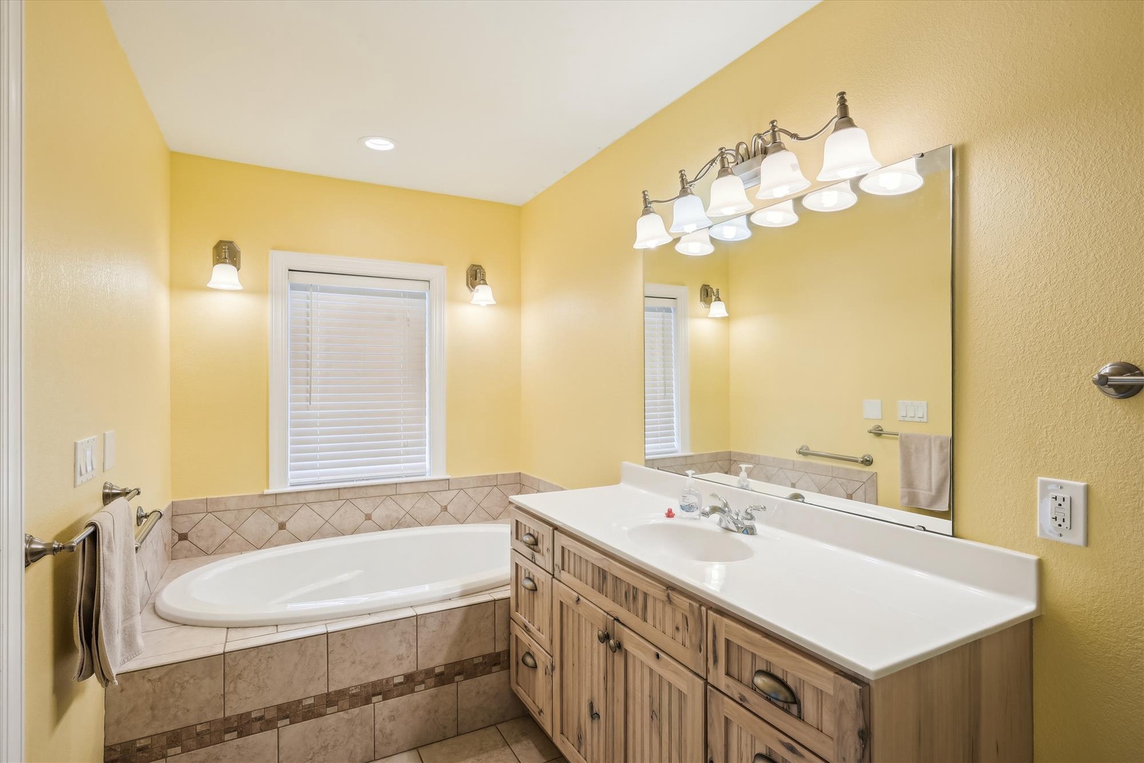 Unwind in your sunny, cheerful bathroom featuring a spacious soaking tub, ample vanity lighting, and warm tile details that invite relaxation after a day of exploring.