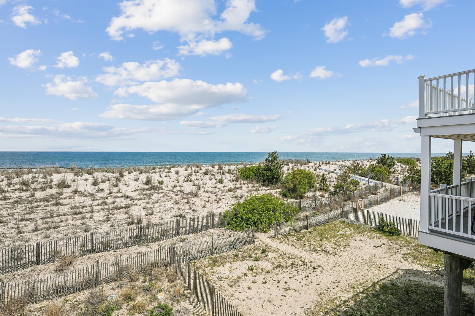 The property sits just steps from pristine sand dunes and the sparkling ocean beyond. Natural dune grasses and wooden fencing frame the beachfront landscape. Open skies and gentle waves set the scene for an unforgettable coastal escape.