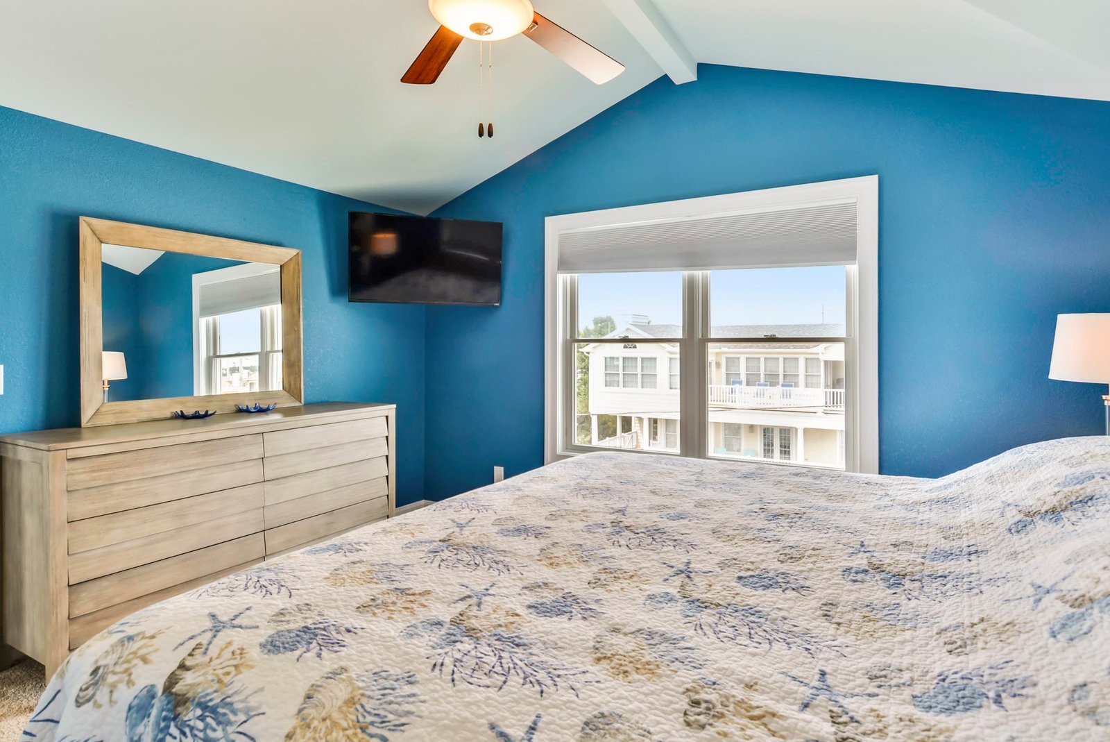 Unwind in your airy bedroom with vaulted ceilings, bold blue walls, and a cozy bed that invites restful sleep after a day of seaside adventures.