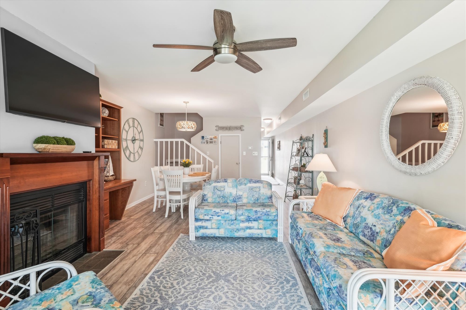 Unwind in your bright, open living space with coastal-blue sofas, a cozy fireplace, and ceiling fan overhead—designed for relaxation and easy beach living.