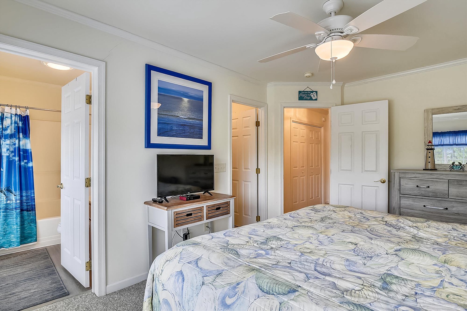 Unwind in your coastal-inspired bedroom with a comfy bed, ceiling fan, flat-screen TV, and calming ocean artwork—your personal retreat after a day of adventure.
