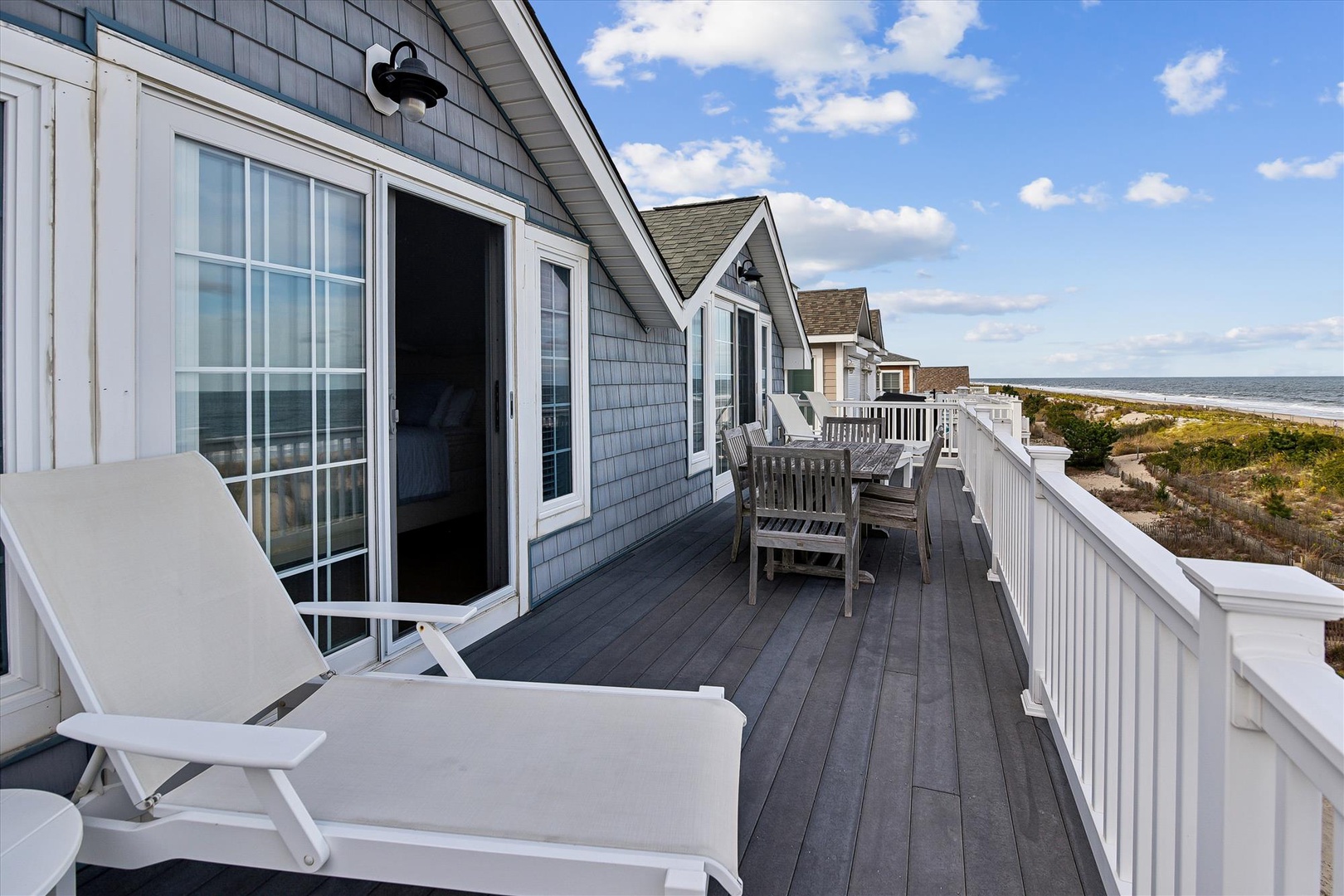 Spacious beachfront deck features lounge chairs and dining space, with direct ocean views stretching to the horizon.