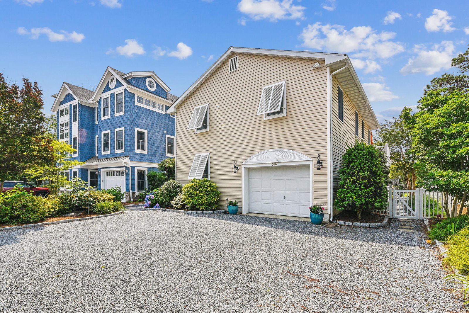 The property features classic coastal architecture with shingled siding and sits within a quiet residential neighborhood, surrounded by mature landscaping and ample parking on a gravel driveway.