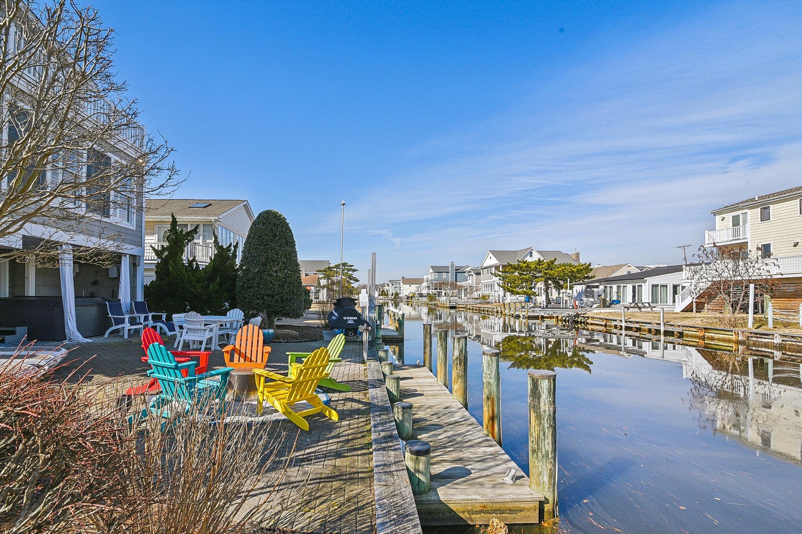 Waterfront vacation rental offering canal access, private dock, and colorful outdoor seating on a sunny winter day. Peaceful residential neighborhood with boat slips.