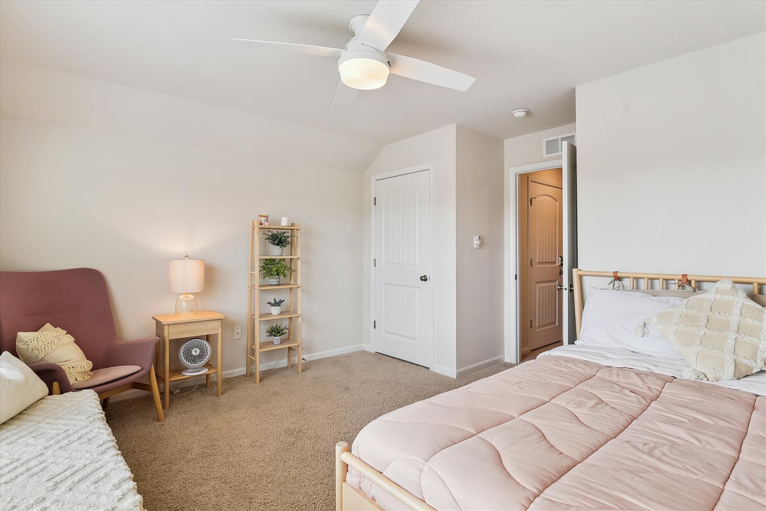 Unwind in your peaceful bedroom sanctuary with a gentle ceiling fan, cozy reading chair, and soft bedding that promises restful nights.