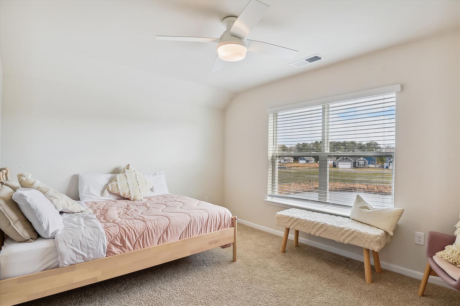 Soft, neutral tones and a plush bed invite you to unwind in comfort. The ceiling fan keeps things breezy, and natural light streams through the wide windows onto your cozy bench.