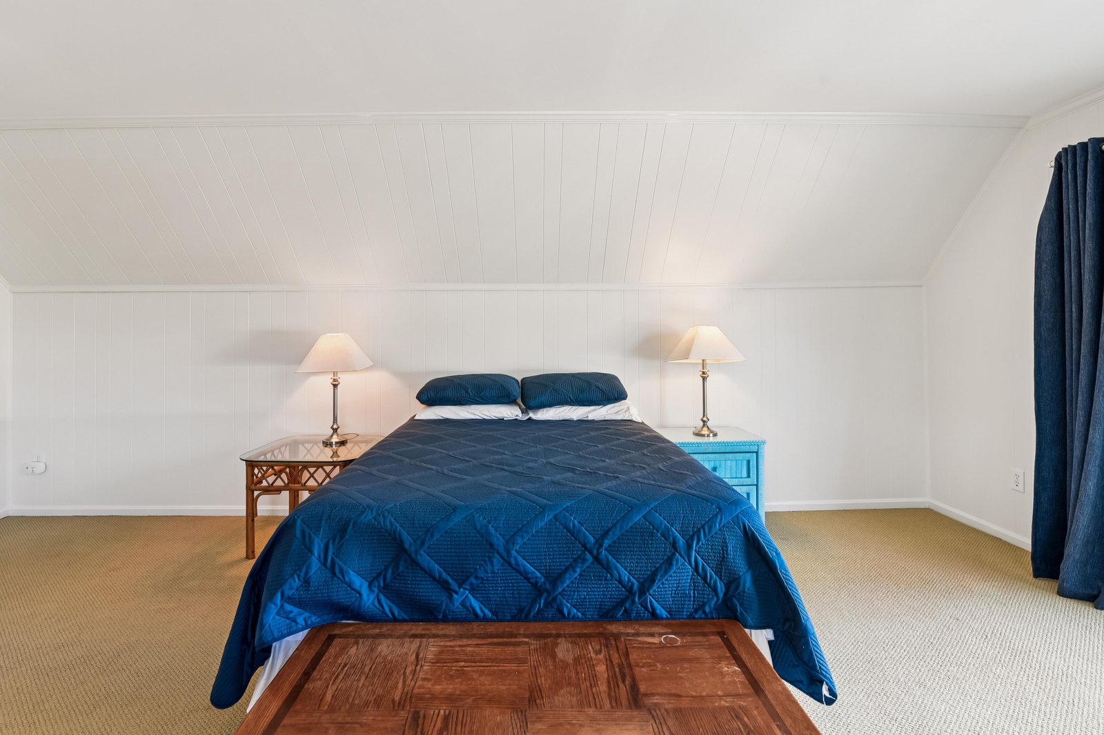 Unwind in this bright, serene bedroom with a plush bed dressed in coastal blues. The sloped ceiling and warm lighting create your own peaceful retreat.