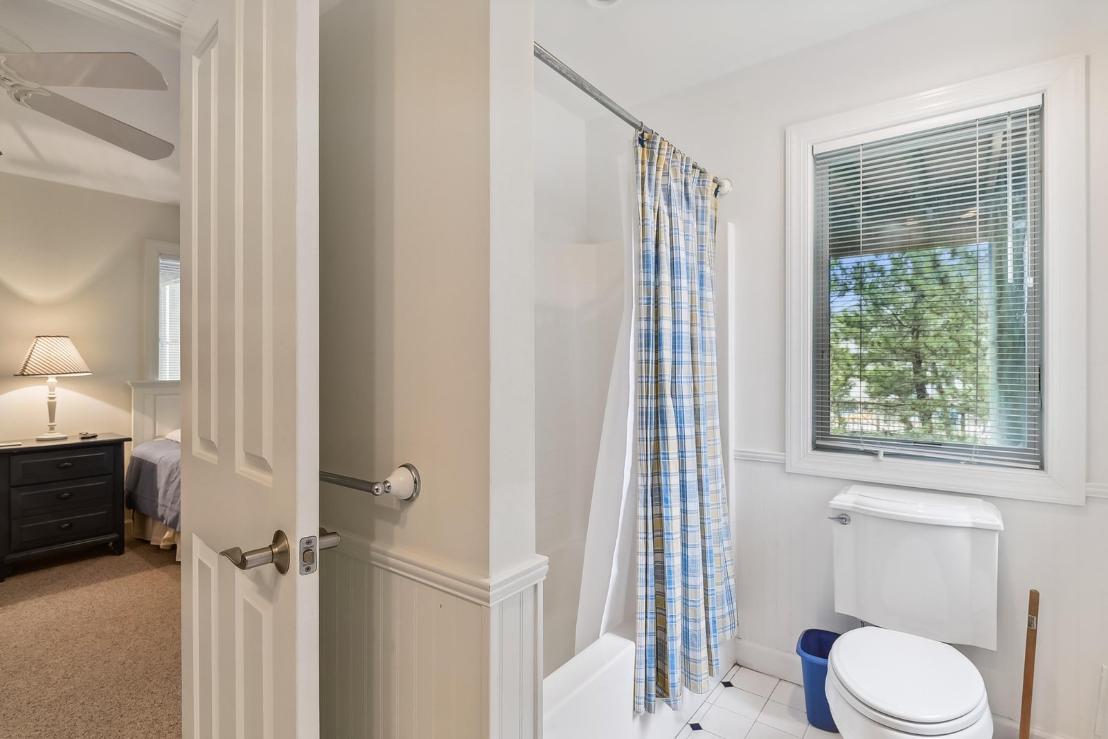 A bright, cheerful bathroom connects to your bedroom for convenient access. The window fills the space with natural light, and the blue plaid curtain adds a cozy, cottage feel to your stay.