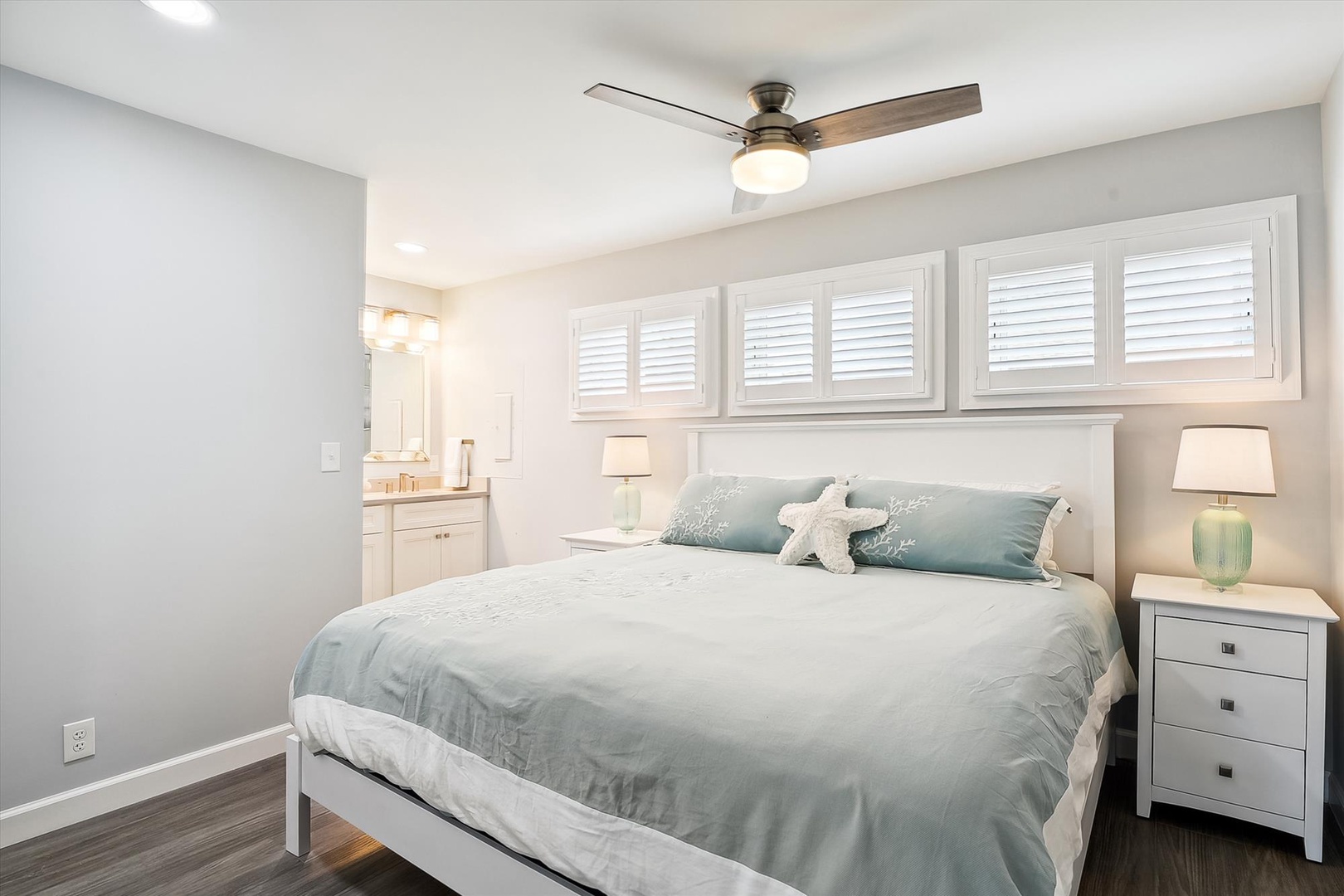 Your bright coastal retreat awaits with a plush bed, gentle ceiling fan, and soft beach-inspired tones. The attached bathroom offers convenience while twin lamps provide warm reading light for peaceful evenings.