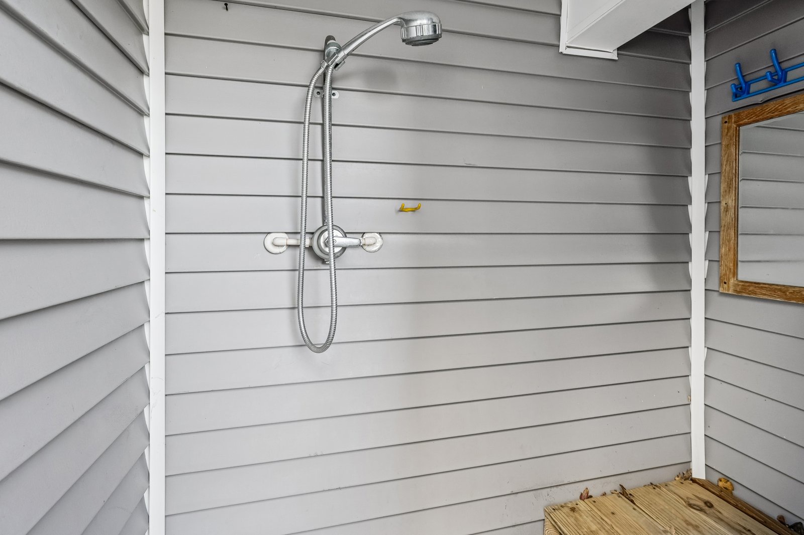 Rinse off after beach days in your private outdoor shower with natural wood flooring and mirror—perfect for refreshing.