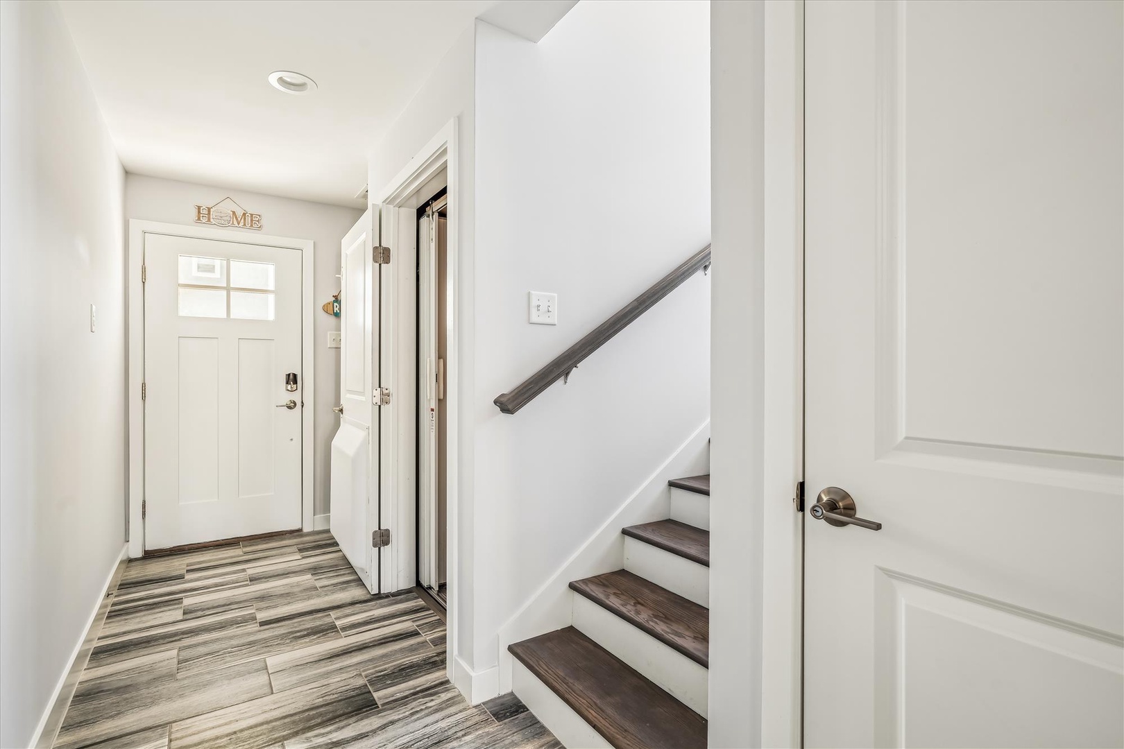 This bright, welcoming entryway features stylish wood-look flooring and a charming staircase, setting the tone for your comfortable stay in this modern, well-maintained home.