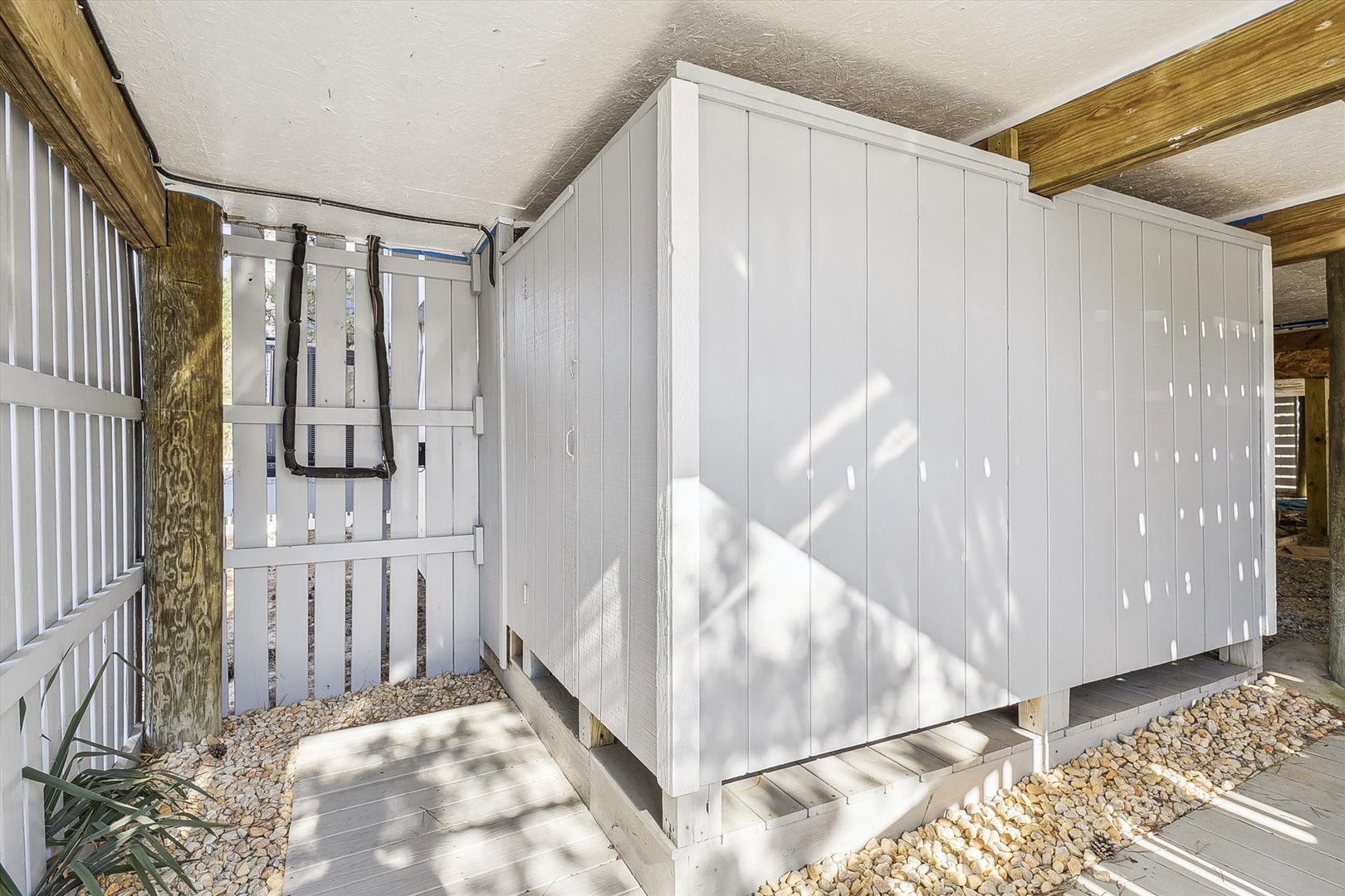 Modern beach cottage exterior with a spacious covered deck and storage, set on a gravel courtyard surrounded by natural wood beams and coastal landscaping.