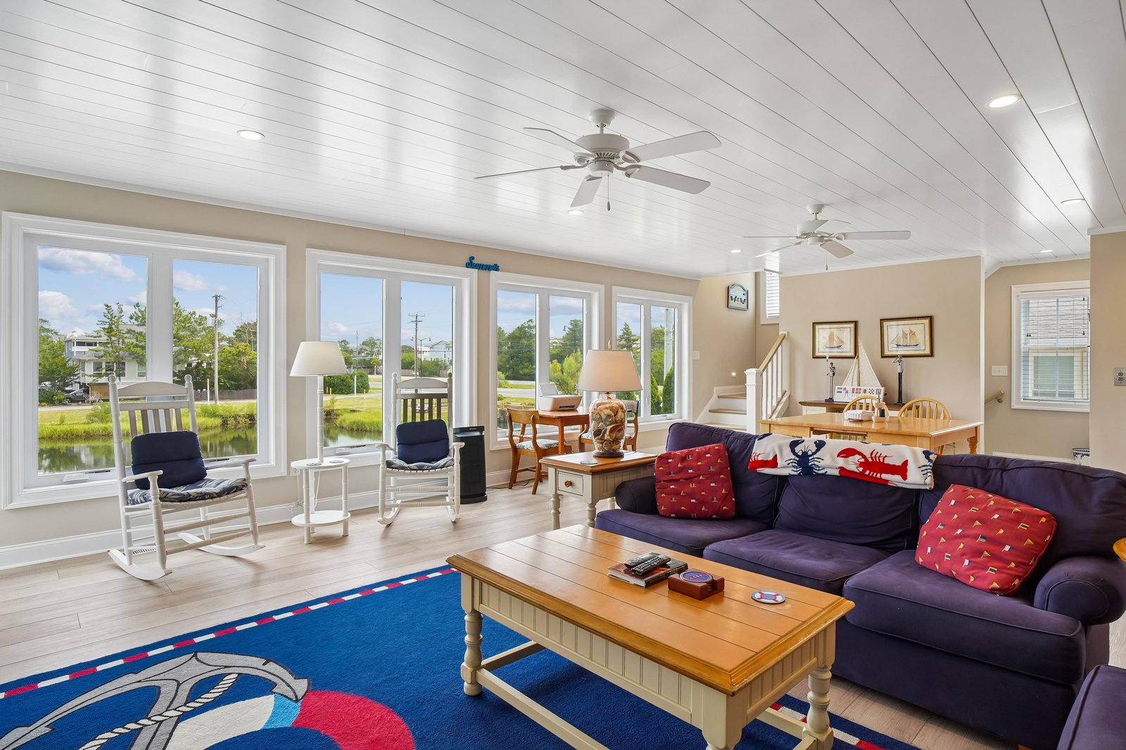 Step into your coastal retreat with nautical charm and sweeping waterfront views framed by floor-to-ceiling windows. Sink into the cozy sofa and let the serene water scene inspire your perfect getaway.