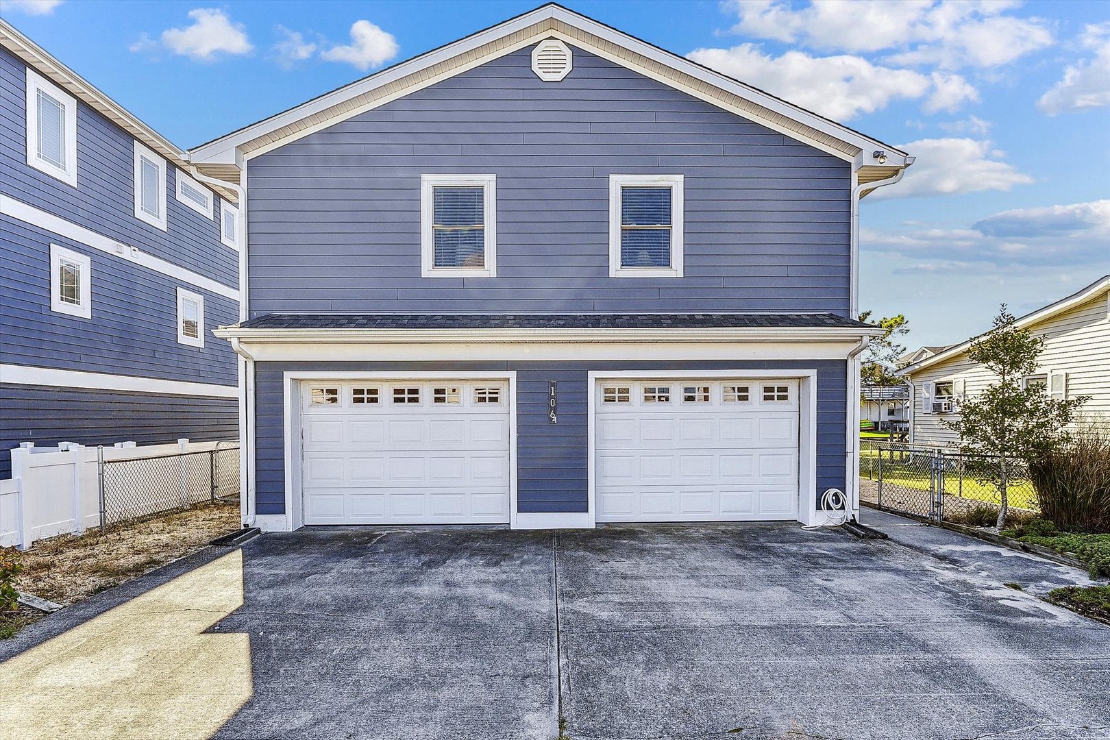 Two-story property with blue siding, white trim, and a two-car garage, located in a quiet residential neighborhood under partly cloudy skies.