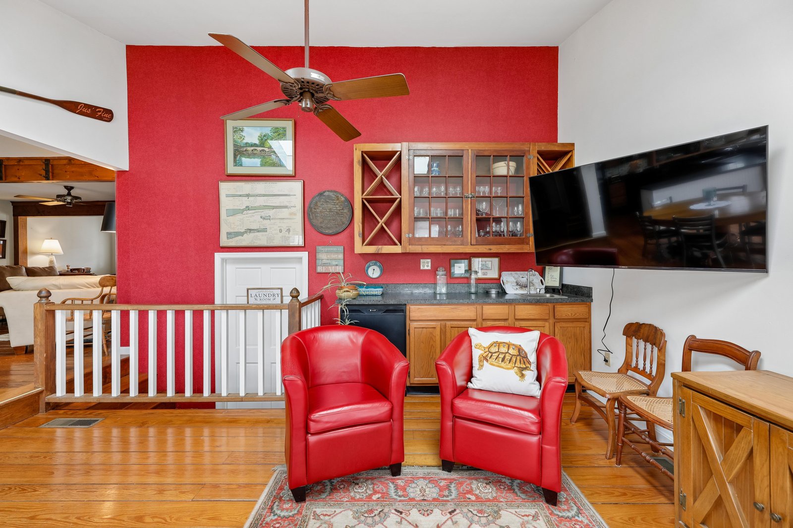 Sink into plush red chairs in this light-filled living room with vaulted ceilings, hardwood floors, and nautical-inspired décor—your perfect spot to relax and unwind.