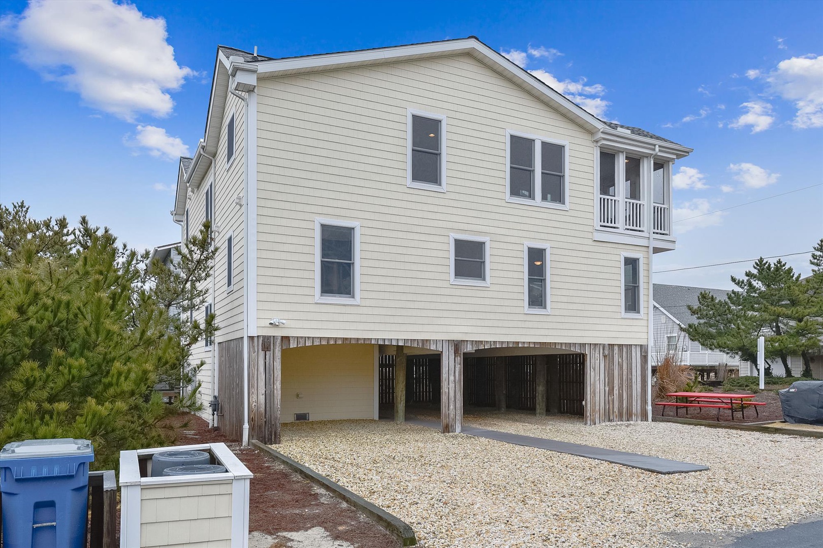 A spacious coastal-style home elevated on stilts, featuring covered parking beneath and a balcony off the upper floor, set in a residential beachside neighborhood.