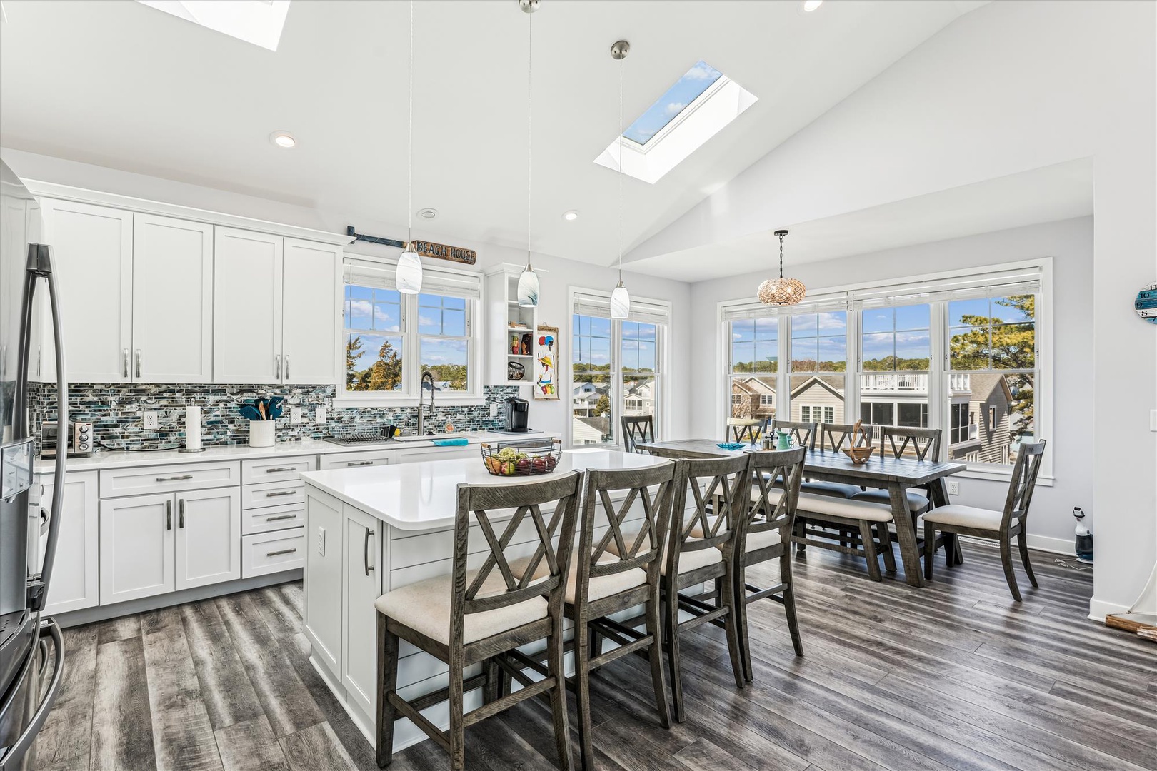 Sunlight pours through soaring skylights into your open-concept kitchen and dining space, where modern white cabinetry meets coastal charm. Gather with loved ones around the island or dining table, enjoying waterfront views.