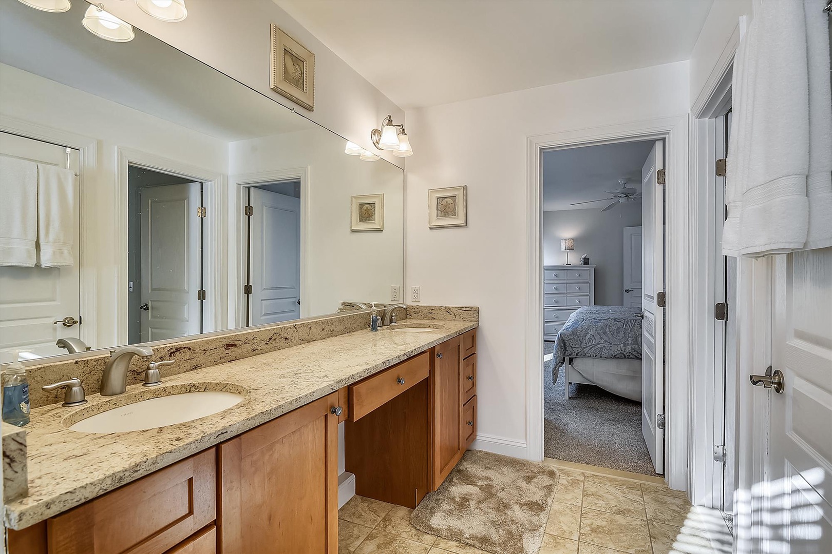 Step into your private en-suite bathroom featuring dual sinks with elegant granite countertops, warm wood cabinetry, and soft lighting. Your restful bedroom awaits just steps away through the connecting door.