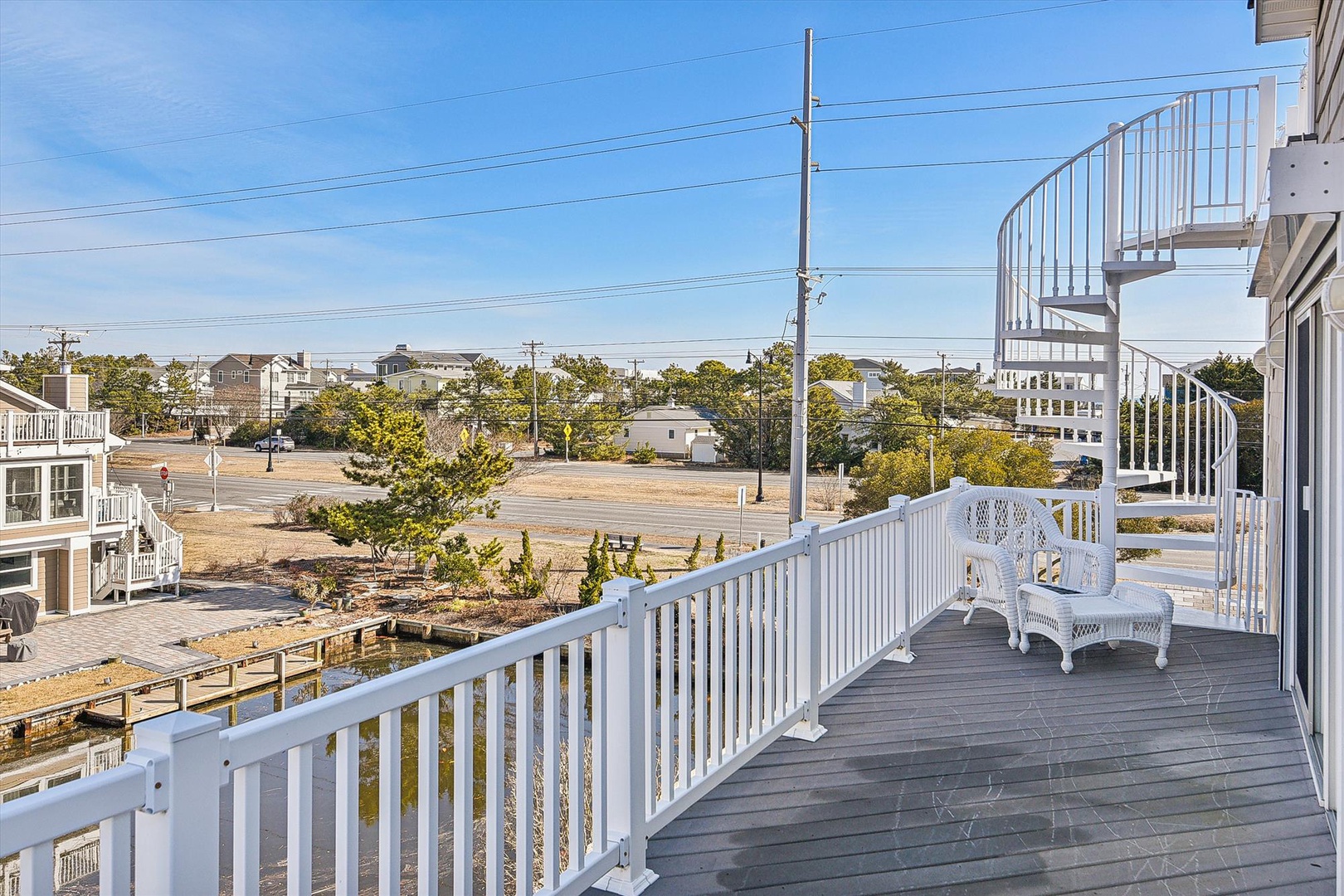 Expansive multi-level deck with scenic views of the surrounding coastal neighborhood, featuring white wicker seating and spiral staircase access.