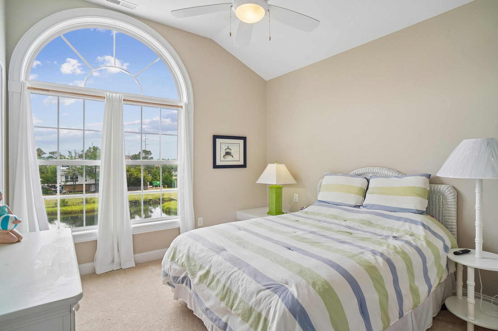 Relax in this bright bedroom with its elegant arched window framing lush waterfront views. Gentle colors and vaulted ceilings create a peaceful retreat for restful nights.