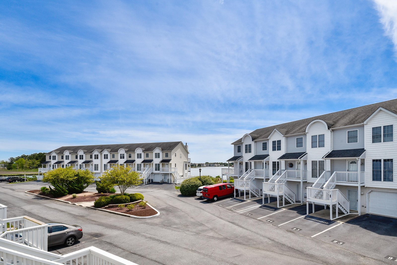 Elevated view of the property complex showing white townhome-style buildings, landscaped grounds, and ample parking for your vehicle throughout the premises.