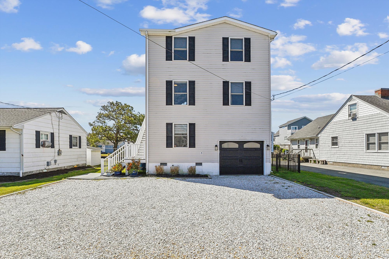 A classic three-story coastal home with black shutters and attached garage, situated in a friendly residential neighborhood with convenient driveway parking.