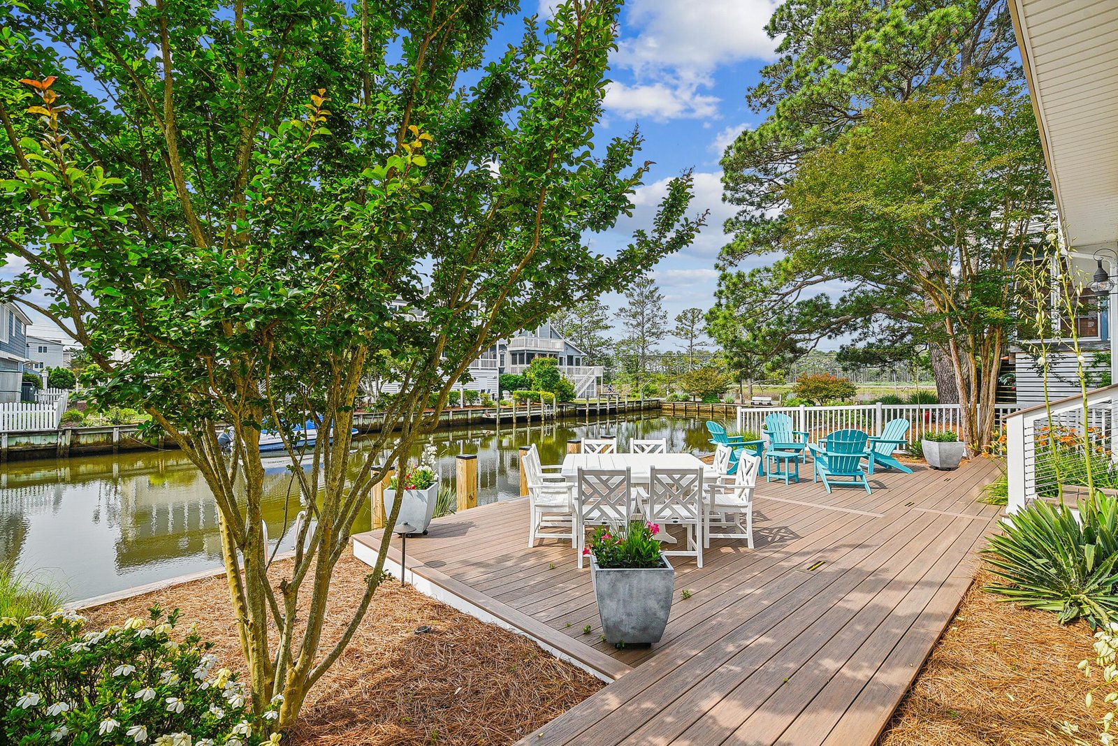 A spacious waterfront deck offers inviting seating and serene views of the canal, surrounded by lush greenery and coastal charm—perfect for morning coffee or evening relaxation.