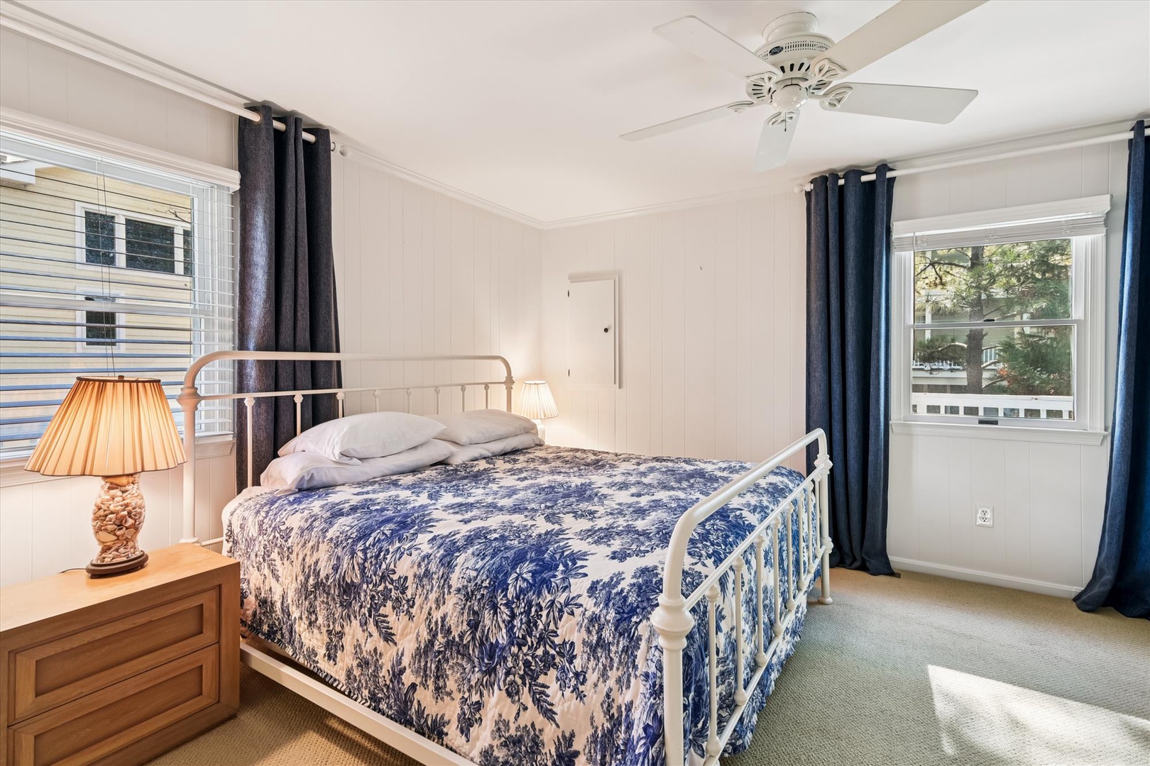 Drift peacefully to sleep in your charming bedroom featuring a cozy iron bed with beautiful blue-and-white linens, gentle ceiling fan, and warm natural light.
