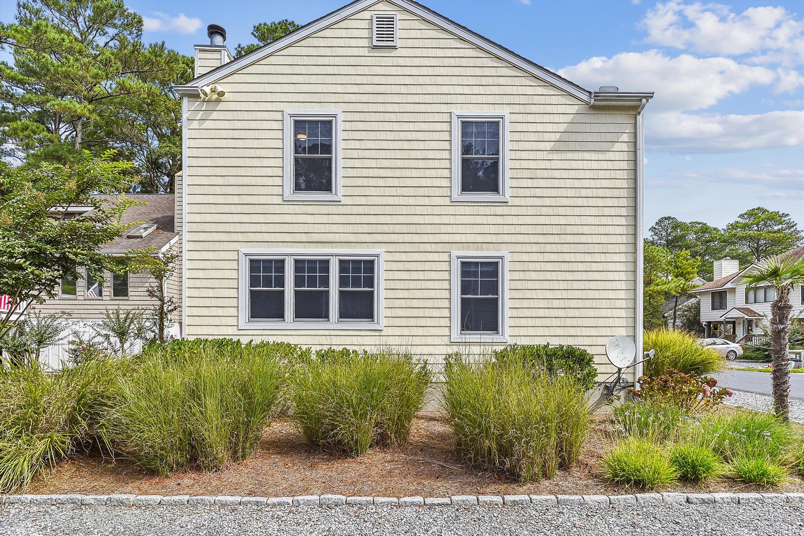 A classic coastal vacation home with light-colored siding and a charming facade, located in a peaceful residential area near the beach and surrounded by mature landscaping.