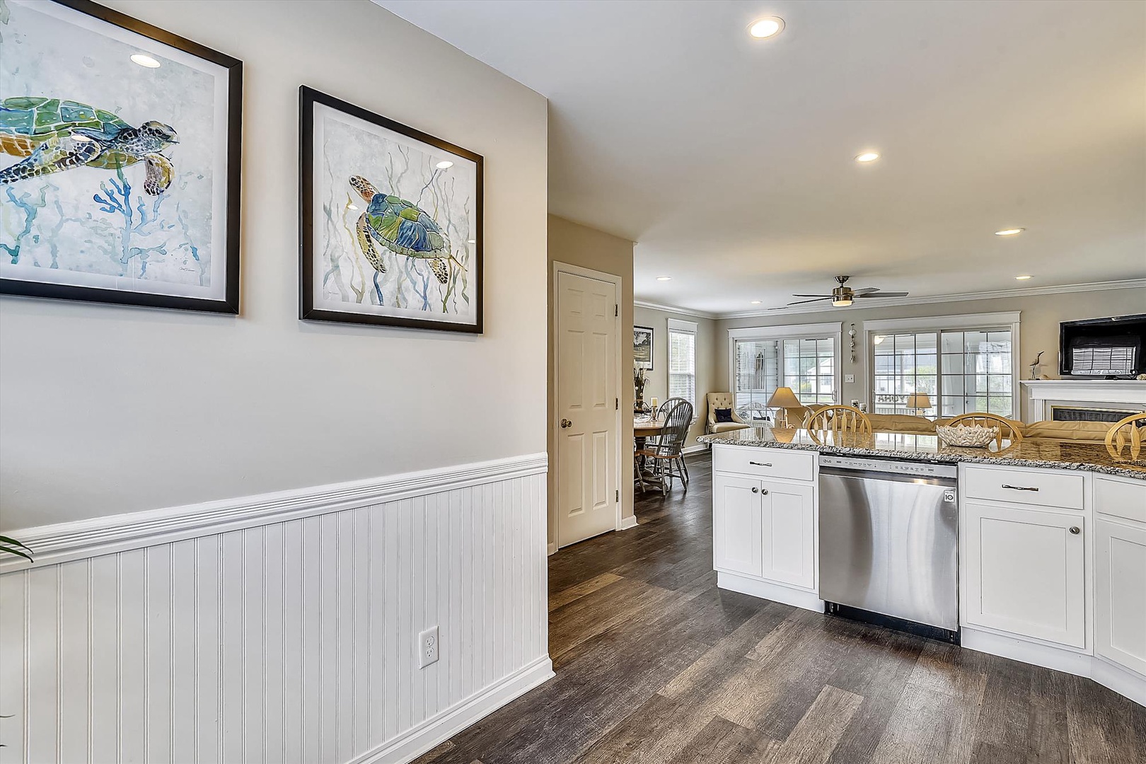 Your coastal-inspired kitchen features bright white cabinetry, modern appliances, and charming sea turtle artwork that sets a relaxing beach house tone throughout the open, sunlit space.