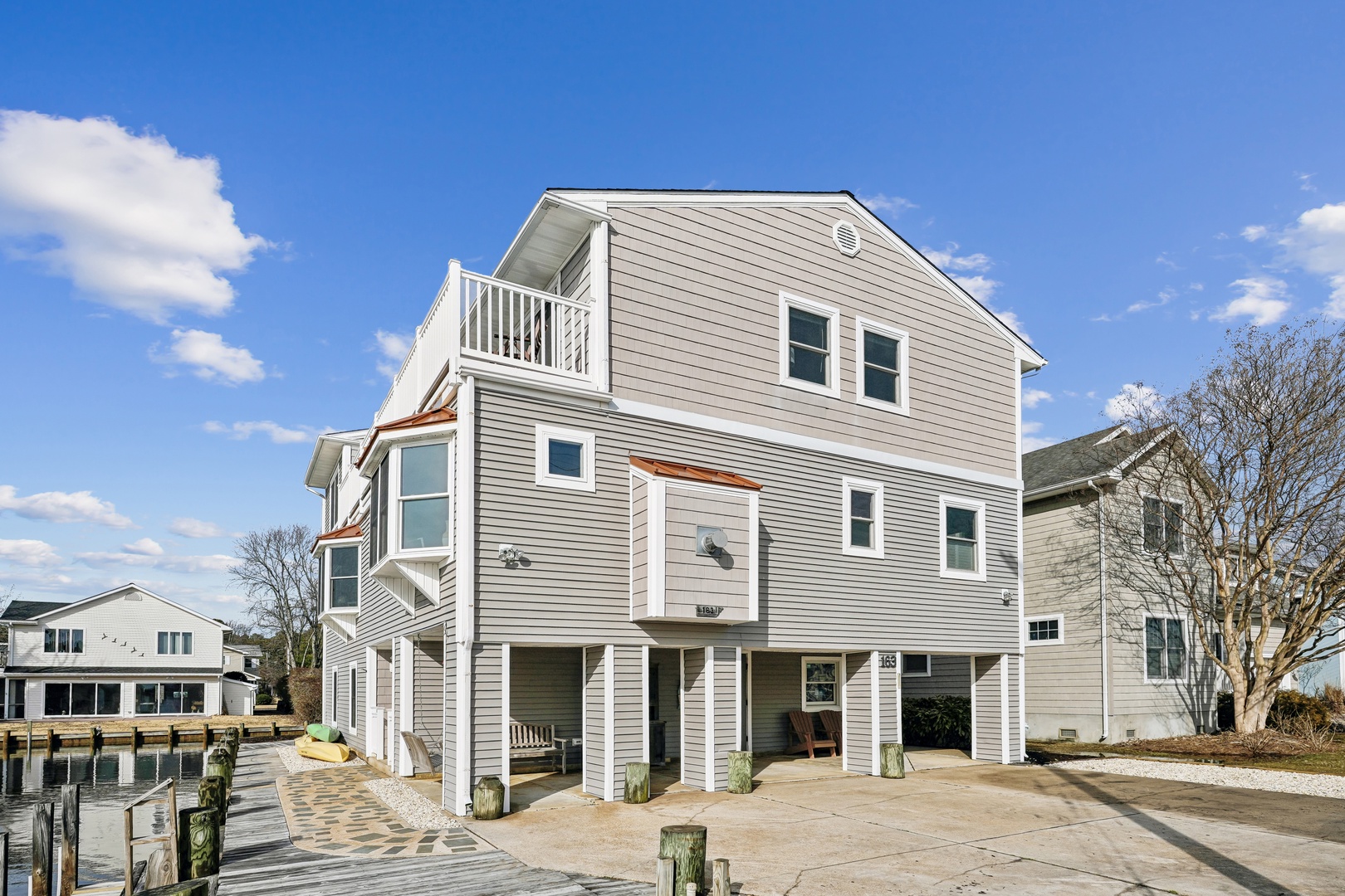 Modern waterfront property featuring gray siding, white trim, and multiple balconies overlooking the peaceful waterside location.