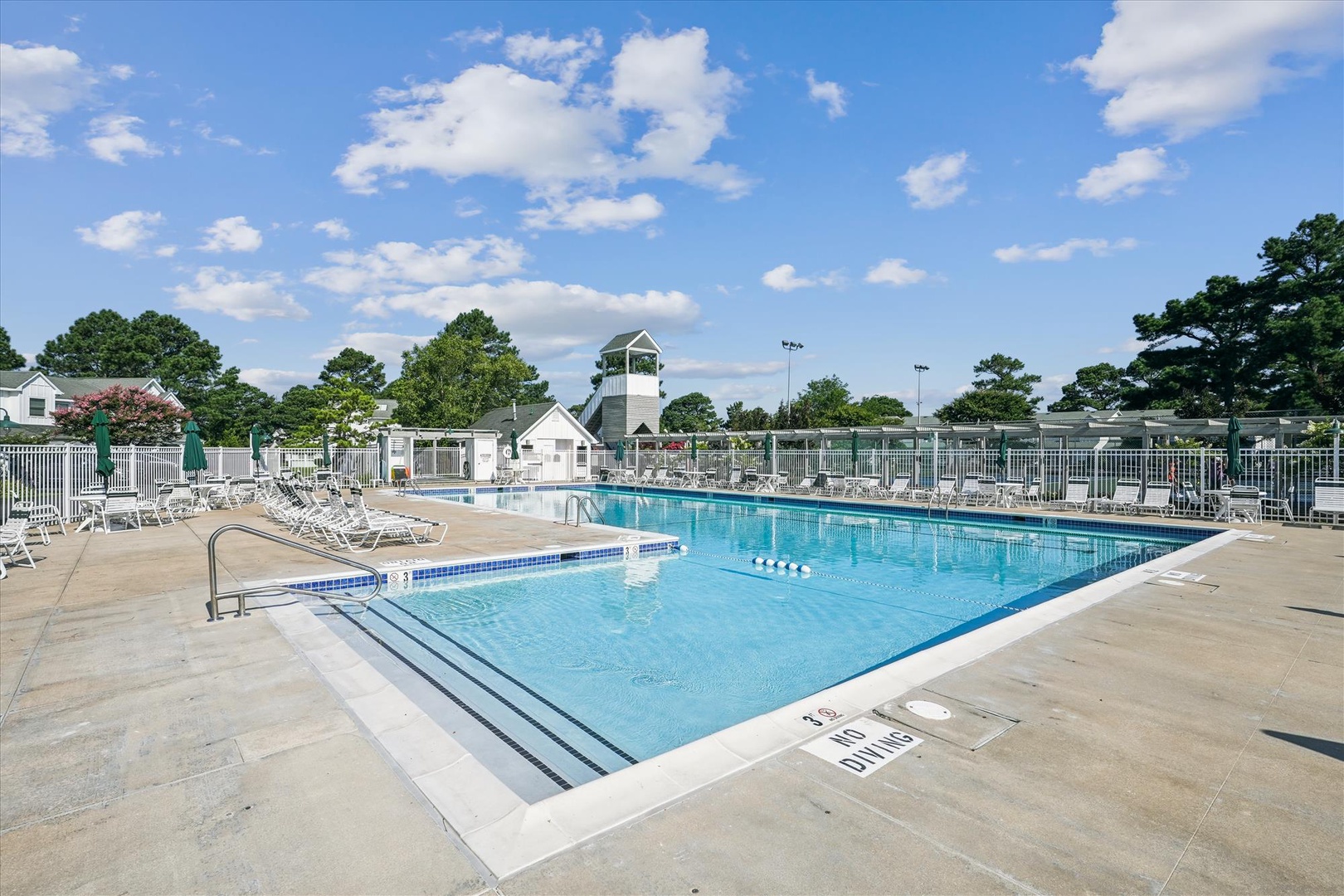 Resort-style community pool area with sparkling blue water, poolside seating, and scenic lighthouse backdrop for perfect relaxation days.
