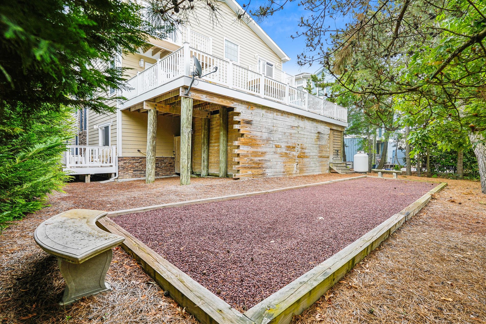 The property features a distinctive two-story structure with covered parking below and a spacious upper-level deck, set among mature trees in a peaceful neighborhood.
